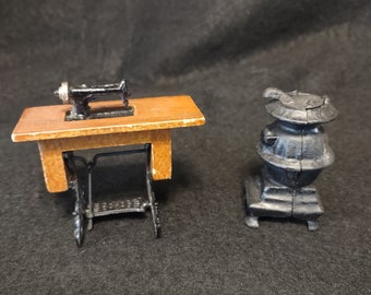 May include: A miniature black cast iron wood-burning stove and a miniature sewing machine on a wooden table with black metal legs.
