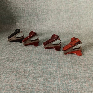 May include: Four staple removers, two red and two black, are lined up on a textured green surface.