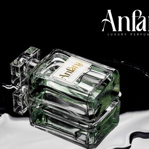 Puede incluir: Un frasco de perfume rectangular de vidrio con una tapa transparente y una etiqueta que dice "Anfana LUXURY PERFUME". El frasco contiene un l&iacute;quido verde y se encuentra sobre una superficie reflectante con un fondo negro.