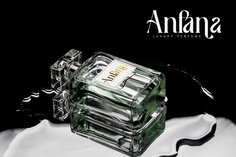 Puede incluir: Un frasco de perfume rectangular de vidrio con una tapa transparente y una etiqueta que dice "Anfana LUXURY PERFUME". El frasco contiene un l&iacute;quido verde y se encuentra sobre una superficie reflectante con un fondo negro.