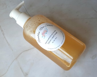 May include: A clear plastic bottle of amber-colored liquid soap with a white pump dispenser. The oval label reads Ramblin' Rose Soaps, Oatmeal Milk & Honey Tallow Liquid Soap, Net Wt. 8oz, Fort Worth, Texas 76114, ramblinrosesoaps.etsy.com.