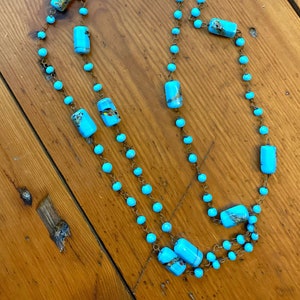 May include: A turquoise blue necklace with rectangular beads and small round beads. The necklace is made of two strands of beads and is strung on a copper wire.