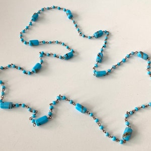May include: A long turquoise blue necklace with small round beads and larger rectangular beads with gold accents.