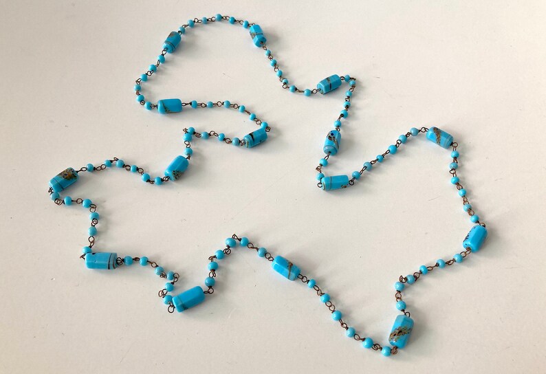May include: A long turquoise blue necklace with small round beads and larger rectangular beads with gold accents.