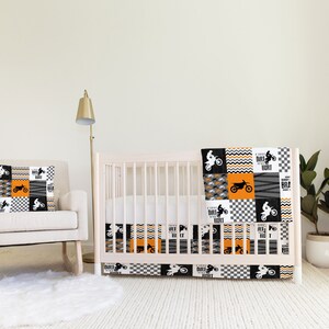 Könnte beinhalten: Ein schwarzes und orangefarbenes Baby-Bettwäsche-Set mit einem Motocross-Thema. Die Bettwäsche hat ein Patchwork-Design mit schwarz-weißen Karos, orange-schwarzen Wellenlinien und schwarzen Silhouetten von Dirtbikes. Der Text "A Little Dirt Never Hurt" ist auf der Bettwäsche gedruckt.