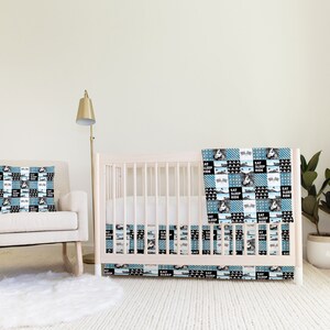 Könnte beinhalten: Ein weißes Babybett mit einem blauen und schwarzen gemusterten Babybettwäsche-Set. Die Bettwäsche hat ein Patchwork-Design mit den Worten "Eat Sleep Ride", die sich durchgehend wiederholen. Das Babybett steht in einem Kinderzimmer mit einem weißen Schaukelstuhl und einer goldenen Stehlampe.