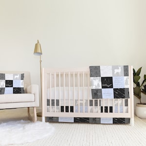Puede incluir: Una cuna blanca con un juego de ropa de cama de cuna de patrón blanco y negro. La ropa de cama presenta un diseño de patchwork con ciervos, árboles y estrellas. Una mecedora blanca con una almohada de patrón blanco y negro se sienta frente a la cuna. Una cortina blanca con un diseño de patrón blanco y negro cuelga en el fondo.