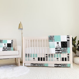 Könnte beinhalten: Ein weißes Babybett mit einem schwarz-weißen gemusterten Bettrock und einer schwarz-weißen gemusterten Bettdecke mit den Worten "Mein Superheld" und "Superhelden-Team". Das Babybett steht in einem Kinderzimmer mit einem Schaukelstuhl und einem weißen Teppich.