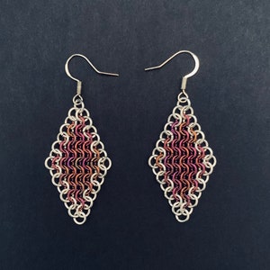 May include: A pair of silver earrings with a diamond-shaped design. The earrings are made of small, interconnected metal rings, with a central section of iridescent purple and pink rings.