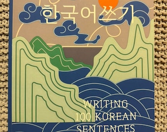 Op de afbeelding: Een boekomslag met een blauwe, groene en oranje illustratie van bergen, wolken en een zon. De titel van het boek is "Writing 100 Korean Sentences" in het Koreaans.