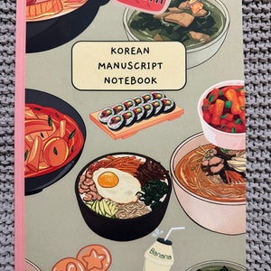 May include: A green notebook with a pink spine. The cover features illustrations of various Korean dishes, including kimchi, bibimbap, and kimbap. The title "Korean Manuscript Notebook" is printed in white on a pink rectangle.