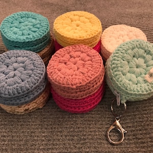 May include: A set of six crocheted coin purses in various colors, including teal, yellow, cream, gray, pink, and green. The green purse has a zipper and a silver key chain attached.