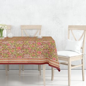 May include: A rectangular dining table with a floral tablecloth featuring a yellow background with pink and green floral patterns. The tablecloth has a red border. Four wooden chairs surround the table, two with white cushions.