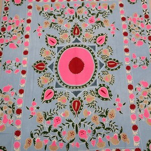May include: A light blue fabric with intricate embroidery featuring pink, red, and green floral designs. The centre of the fabric features a large pink circle with a red centre.