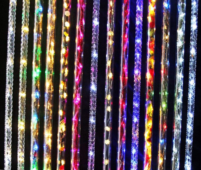May include: A collection of clear, textured tubes with embedded LED lights. The lights are various colors, including white, green, yellow, red, and blue. The tubes are arranged vertically against a black background, creating a vibrant display.
