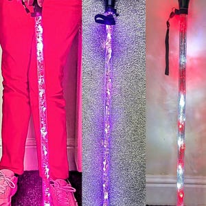 May include: Light-up walking canes with black handles and clear shafts filled with decorative elements. The canes feature LED lights in pink, purple, and red and white. The canes are designed for mobility and visibility.