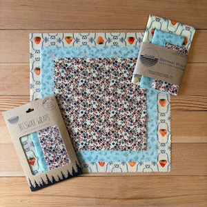 May include: A set of square beeswax wraps featuring various patterns including strawberries, blueberries, and blue floral motifs. The packaging includes the text BEESWAX WRAPS and lists sizes of 20x20, 25x25, and 30x30 cm on the cardboard sleeve.