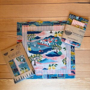 May include: A set of three beeswax wraps with assorted patterns including a coastal village scene with lemons, pink stripes, and blue sardine motifs. The packaging features the text SHOR Beeswax Wraps Earth Friendly Food Storage.