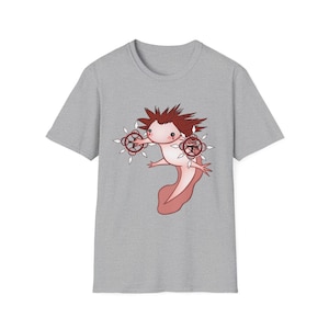 May include: A light gray t-shirt featuring a cartoon axolotl with red hair and a pink body. The axolotl is holding two circular objects with white accents. The design is centered on the shirt.