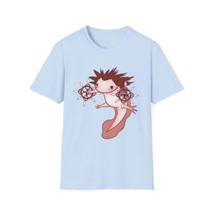 May include: Pale blue t-shirt with a cartoon axolotl design. The axolotl has spiky brown hair and decorative elements. The axolotl is pink and white with a red tail. The design is centered on the front of the shirt.