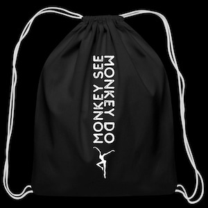 May include: Black drawstring backpack with white text reading "MONKEY SEE MONKEY DO" vertically, and a white silhouette of a person doing a ballet pose. The bag has white drawstrings.