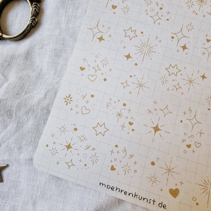 May include: A sheet of gold glitter stickers with various designs, including stars, hearts, and fireworks. The stickers are on a white gridded background. The text "moehrekunst.de" is printed in the bottom right corner.