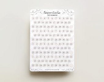 May include: A sheet of white sticker paper with black numbers 1 through 31 printed on it. The numbers are arranged in rows of ten, with the numbers 1-11 on the top row, 12-21 on the second row, and 22-31 on the third row. The sticker paper is surrounded by a decorative border of stars and plus signs.