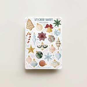 Könnte beinhalten: Ein Stickerbogen mit verschiedenen Weihnachtsschmuck. Der Bogen enthält einen Lebkuchenmann, eine Glocke, einen Stern, eine Schneeflocke und Kugeln in Rot, Grün, Gold und Blau. Der Text "STICKER SHEET tree ornaments" steht oben.