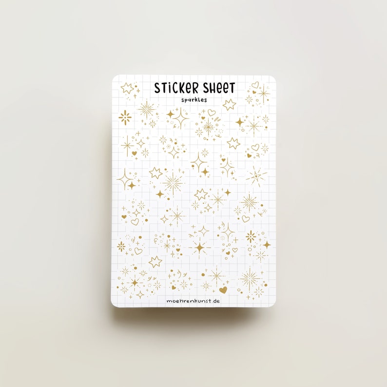 May include: A sticker sheet with gold glitter and sparkle designs. The sheet has a white background with a grid pattern. The text "STICKER SHEET" and "sparkles" is printed in black at the top of the sheet. The text "mohrenkunst.de" is printed in black at the bottom of the sheet.