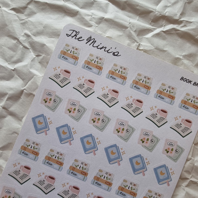 Puede incluir: Una hoja de pegatinas con ilustraciones de libros, tazas de caf&eacute; y estrellas. Las pegatinas est&aacute;n sobre un fondo blanco y tienen una combinaci&oacute;n de colores azul claro, rosa y verde. El texto "The Mini's" y "BOOK BR" est&aacute; impreso en la hoja.