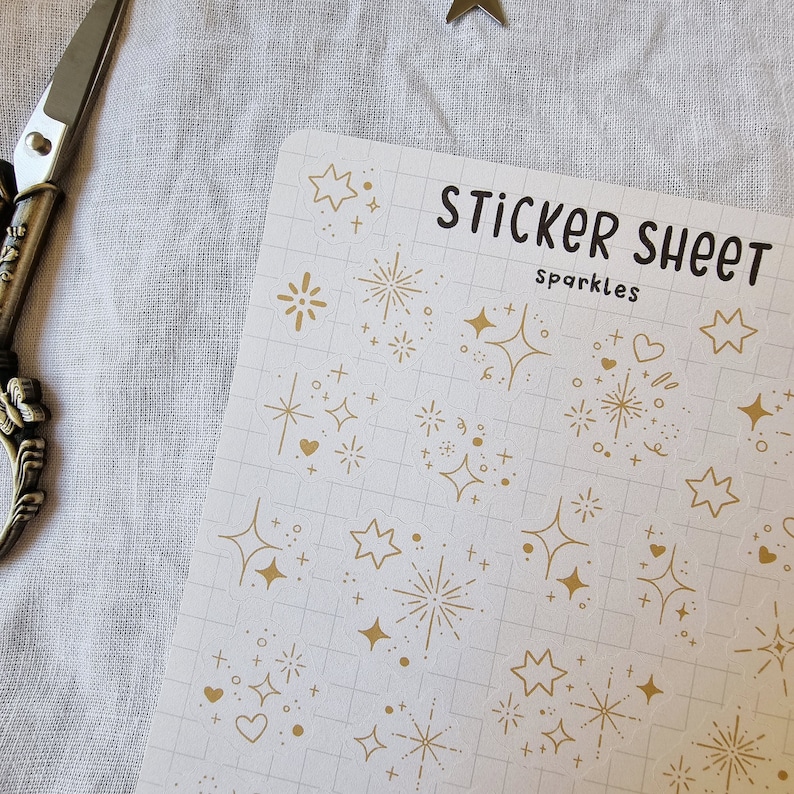 May include: A sheet of gold glitter stickers with various designs, including stars, hearts, and fireworks. The sheet is labeled "Sticker Sheet Sparkles".