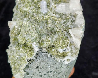 May include: A natural mineral specimen featuring a combination of colors and textures. The top portion is covered in small, light green crystals and larger, clear, crystalline formations. The bottom section is a smooth, gray-green color.