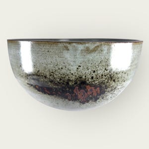 Peut inclure: Un grand bol rond en céramique avec un glaçage moucheté dans les tons gris, noir et brun. Le bol a un bord légèrement irrégulier et une finition lisse et brillante.