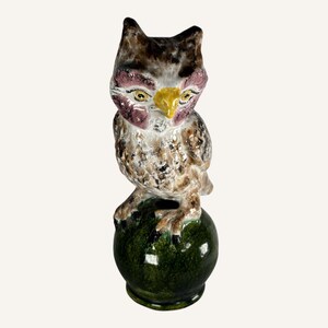 May include: A ceramic owl figurine with brown, white, and yellow painted details. The owl is perched on a green ball.