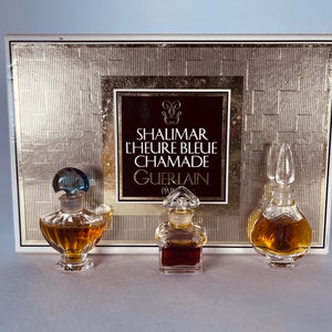Puede incluir: Un conjunto de tres frascos de perfume en miniatura en una caja dorada. Los frascos están etiquetados "Shalimar L'Heure Bleue Chamade Guerlain Paris".