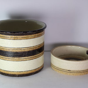 Peut inclure: Un ensemble de deux récipients en céramique avec un motif rayé en brun, beige et blanc. Le plus grand récipient est plus haut et a une forme cylindrique. Le plus petit récipient est plus court et a une forme ronde.