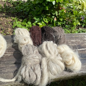 Puede incluir: Cinco ovillos de hilo en varios tonos de blanco y marrón. El hilo está dispuesto sobre una superficie de madera.