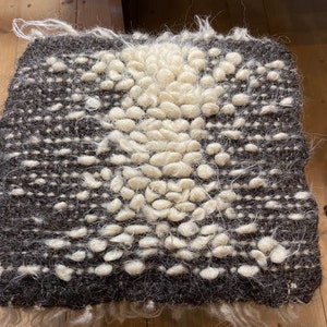 Pode incluir: Um tapete tecido marrom e branco com um design texturizado em relevo. O tapete tem um centro branco com uma borda marrom.