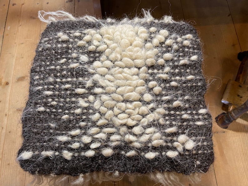 Pode incluir: Um tapete tecido marrom e branco com um design texturizado em relevo. O tapete tem um centro branco com uma borda marrom.