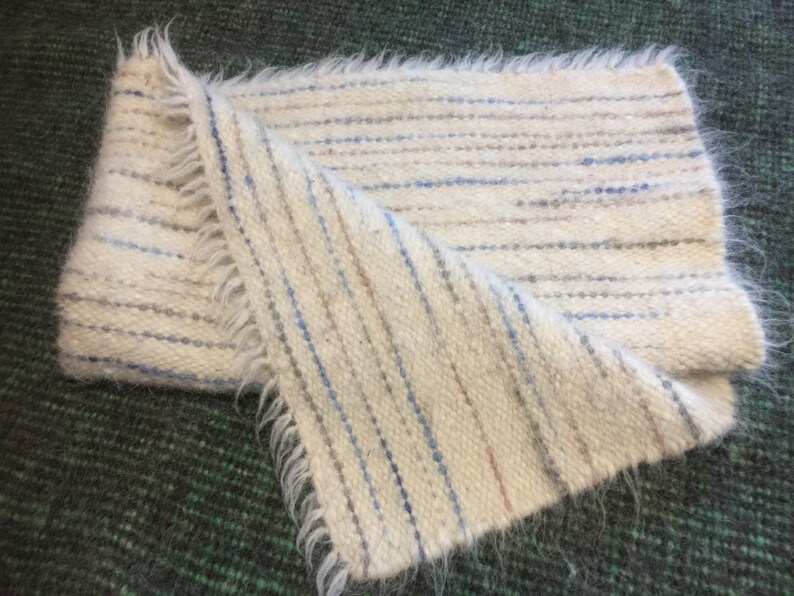 May include: A white woven throw blanket with blue and brown stripes. The blanket has a fringed edge.