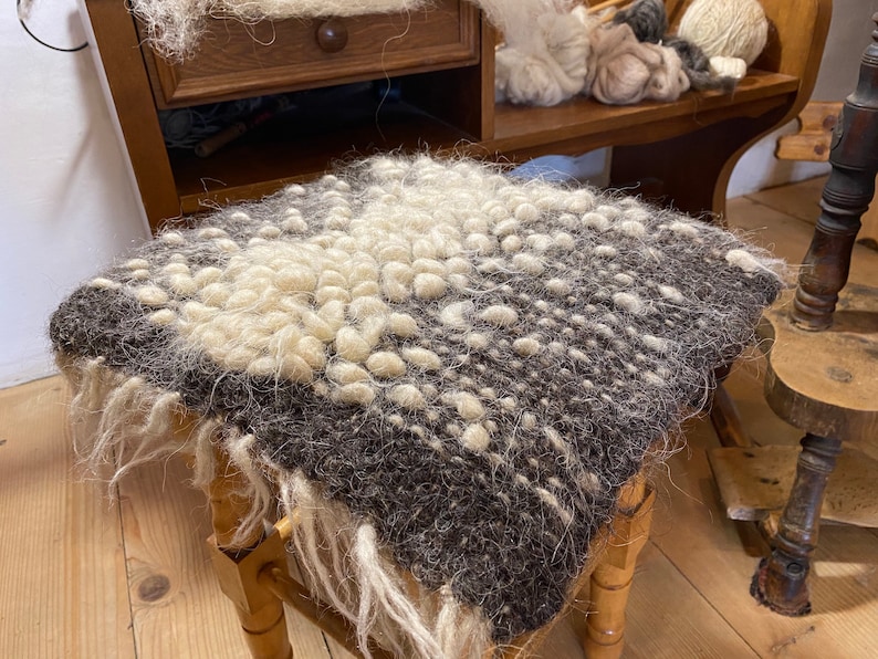 Pode incluir: Um close-up de um almofada de l&atilde; marrom e branco com uma superf&iacute;cie texturizada. A almofada est&aacute; sentada em um banquinho de madeira.