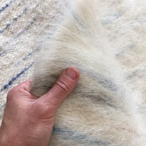 May include: A close-up of a white and blue striped woven fabric with a soft, fluffy texture. The fabric is being held by a hand.
