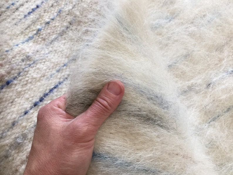 May include: A close-up of a white and blue striped woven fabric with a soft, fluffy texture. The fabric is being held by a hand.