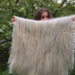 May include: A white and blue fuzzy blanket with a fringed edge. The blanket is being held up by a person.