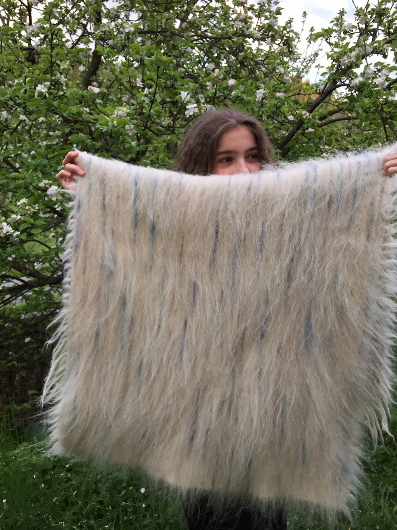 May include: A white and blue fuzzy blanket with a fringed edge. The blanket is being held up by a person.