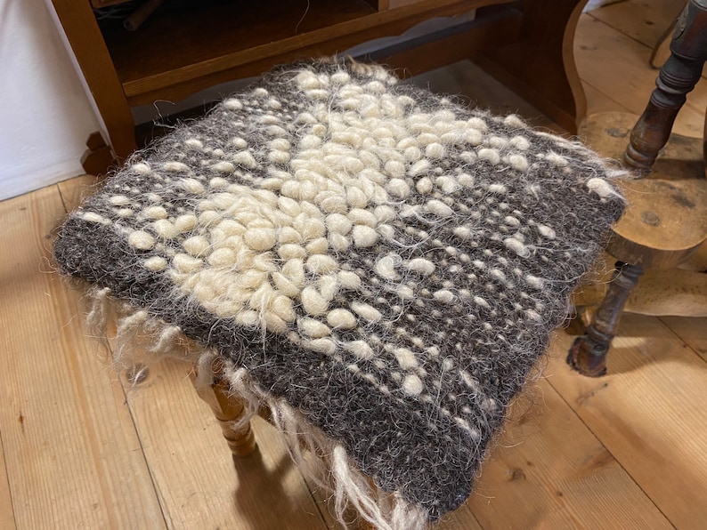 Pode incluir: Um almofada tecido marrom e branco com uma superf&iacute;cie texturizada. O almofada &eacute; feito de l&atilde; e tem uma franja ao redor das bordas.