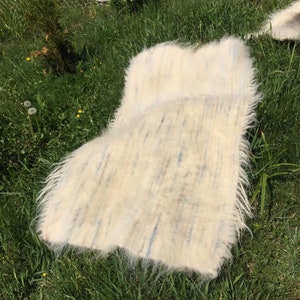 May include: A white fluffy rug with blue and brown streaks laid out on green grass.