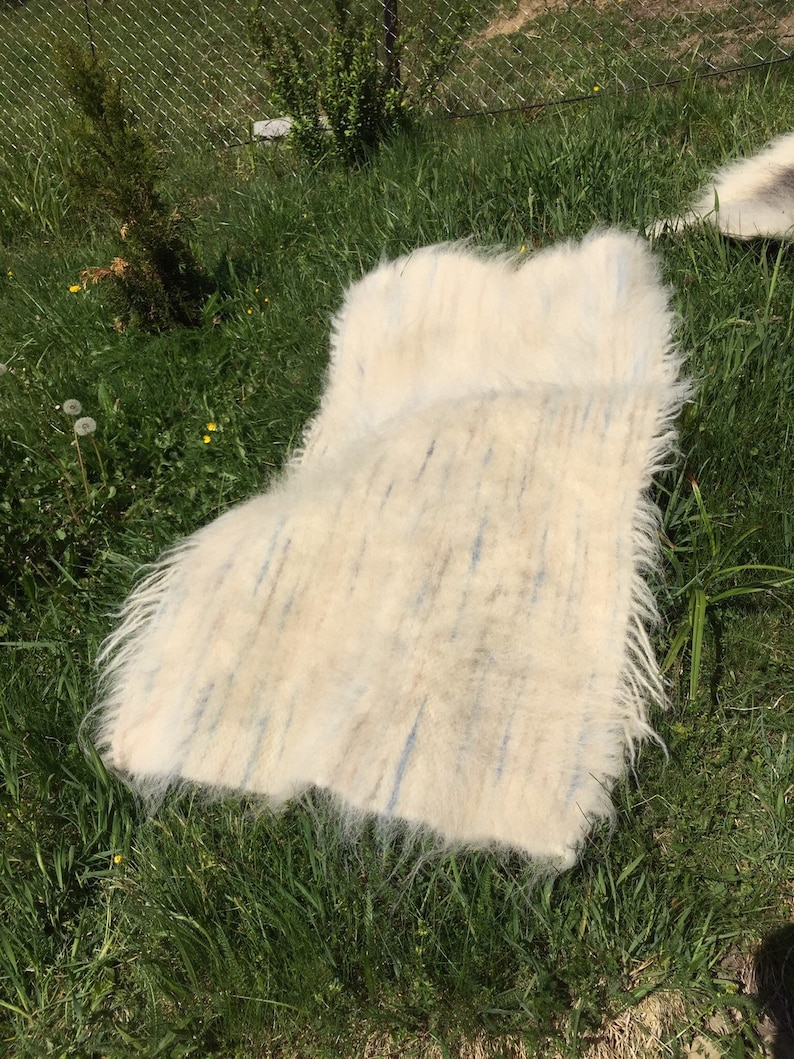 May include: A white fluffy rug with blue and brown streaks laid out on green grass.