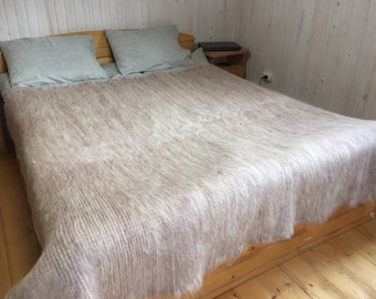 May include: A soft, light brown and white blanket with a fuzzy texture is spread across a bed with two gray pillows. The bed is made of wood and has a wooden headboard.