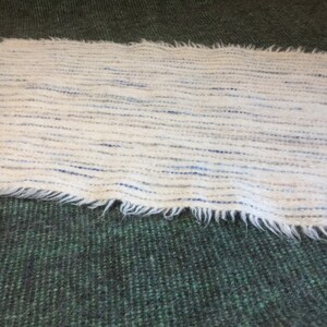 May include: A white woven rug with blue and gray stripes. The rug has a fringed edge and is made of a soft, fluffy material.